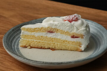 One small Japanese strawberry shortcake on a stylish Japanese plate on a wooden tray on a black cloth on a white table