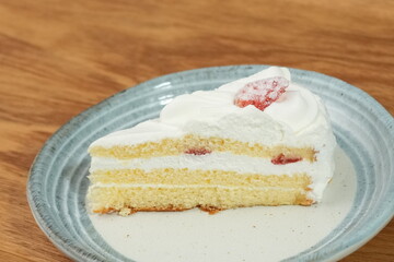 One small Japanese strawberry shortcake on a stylish Japanese plate on a wooden tray on a black cloth on a white table
