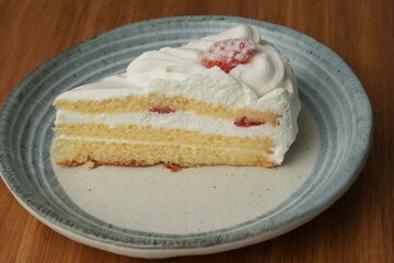 One small Japanese strawberry shortcake on a stylish Japanese plate on a wooden tray on a black cloth on a white table