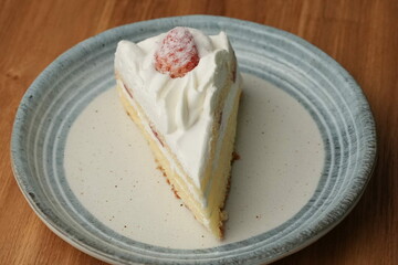One small Japanese strawberry shortcake on a stylish Japanese plate on a wooden tray on a black cloth on a white table