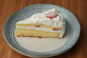 One small Japanese strawberry shortcake on a stylish Japanese plate on a wooden tray on a black cloth on a white table
