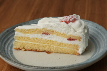 One small Japanese strawberry shortcake on a stylish Japanese plate on a wooden tray on a black cloth on a white table