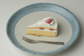 One small Japanese strawberry shortcake and a big fork on a stylish big plate on a white table