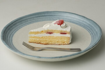 One small Japanese strawberry shortcake and a big fork on a stylish big plate on a white table