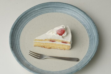 One small Japanese strawberry shortcake and a big fork on a stylish big plate on a white table