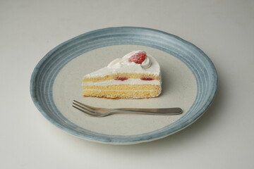 One small Japanese strawberry shortcake and a big fork on a stylish big plate on a white table