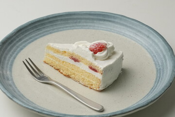 One small Japanese strawberry shortcake and a big fork on a stylish big plate on a white table
