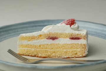 One small Japanese strawberry shortcake and a big fork on a stylish big plate on a white table