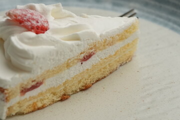One small Japanese strawberry shortcake and a big fork on a stylish big plate on a white table