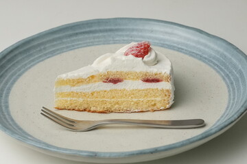 One small Japanese strawberry shortcake and a big fork on a stylish big plate on a white table