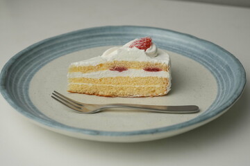 One small Japanese strawberry shortcake and a big fork on a stylish big plate on a white table
