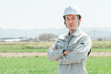 田舎の田んぼに立つ作業着姿のミドル世代の作業員・職人・現場監督
