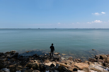 An unidentified angler fishing on a rocky patch in front of the Malacca Straits Sea, Malaysia