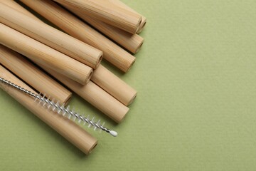 Bamboo drinking straws and cleaning brush on green background, top view. Space for text