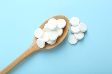 Antibiotic pills and spoon on light blue background, flat lay