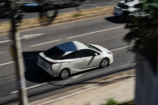 White Toyota Prius in city street, Hybrid Sedan in movement, car driving