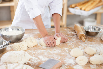 Female baker in uniform kneading raw dough close-up