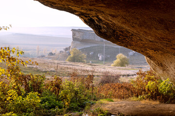 View from inside cave in mountainous area at sunset, autumn. In distance you can see table...