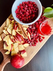 white bowl full of cranberries and apple slices on cutting board, ingredients for making fruit drink