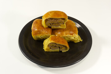 Bolen Pisang is a light dish made from bananas covered in rolled sheets of pastry dough. Various toppings such as cheese and chocolate. Served in black plate on white background. Selective focus image