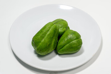 Sechium edule or fresh chayote on white plate isolated on white background. Food ingredient, vegetarian cuisine, organic farm plant