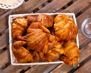 Dark brown baked croissant with delicate and juicy filling. Pastries are stacked in wicker basket, standing on wooden table, outdoor cafe - bakery -burger joint, snack on go