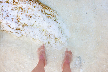 Fototapeta premium A person's feet are in the water, and the sand is white