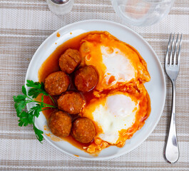 Appetizing fried eggs with meatballs served on plate for breakfast..
