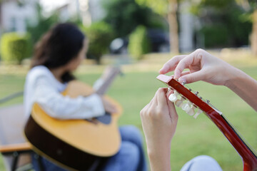 Close up of hand fine-tuning acoustic guitar, Asian kid girl playing guitar with friend in the park