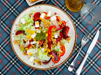 Appetizing salad of fresh vegetables served with feta cheese and pesto on plate