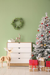 Beautiful Christmas tree with gift boxes and chest of drawers near green wall
