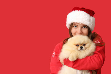 Young woman in Santa hat with cute Pomeranian dog on red background