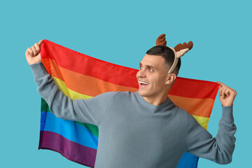 Young man in reindeer horns with LGBT flag on blue background