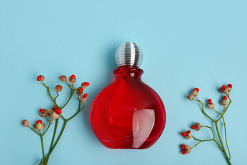 Composition with red bottle of perfume and flowers on blue background