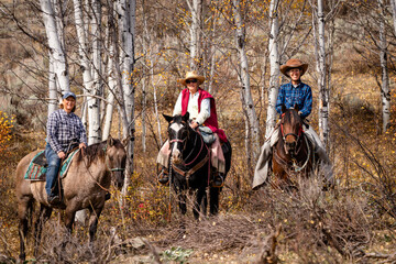 three women riding horses in the forest mountains in the fall