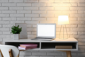 Comfortable workplace with modern laptop and glowing lamp on table