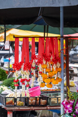 Vibrant decorations of fresh flowers hang from stalls at a bustling street market in Thailand, showcasing brilliant colors and local craftsmanship amidst the lively atmosphere.