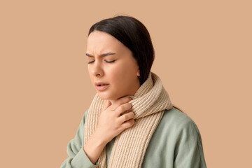 Beautiful young woman in scarf suffering from sore throat on brown background