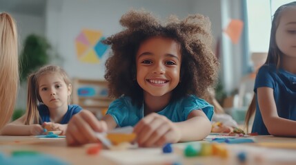 Fototapeta premium A young girl with curly hair smiles at the camera while working on a craft project with her classmates.