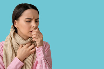Beautiful young woman in scarf suffering from sore throat on blue background