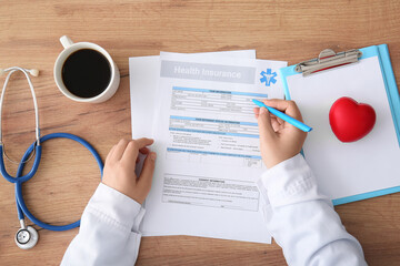 Female doctor hands filling health insurance form near cup of coffee and stethoscope on table
