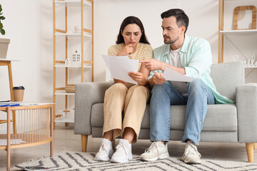 Upset young couple looking through documents at home. Bankruptcy concept