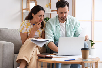 Young couple using laptop to pay bills at home. Bankruptcy concept