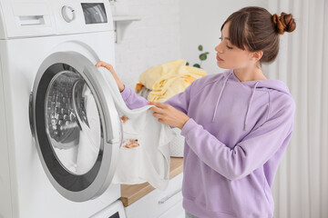 Young woman putting stained clothes into washing machine in laundry room