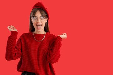 Fashionable young woman in red clothes celebrating success on color background