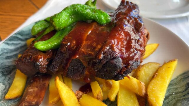 Tasty bbq pork ribs with green Spanish padron peppers and french fries, bbq sauce on grilled meat in Spain, 4K shot