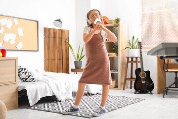Cute little girl with headphones and microphone singing at home
