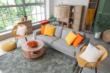 Stylish interior of living room with sofa, armchairs and apricots in bowl on coffee table