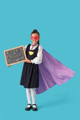 Fototapeta premium Happy schoolgirl dressed as superhero holding blackboard with text BACK TO SCHOOL on blue background