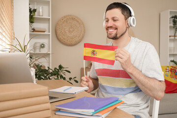 Handsome man in headphones with flag of Spain learning language online at home © Pixel-Shot
